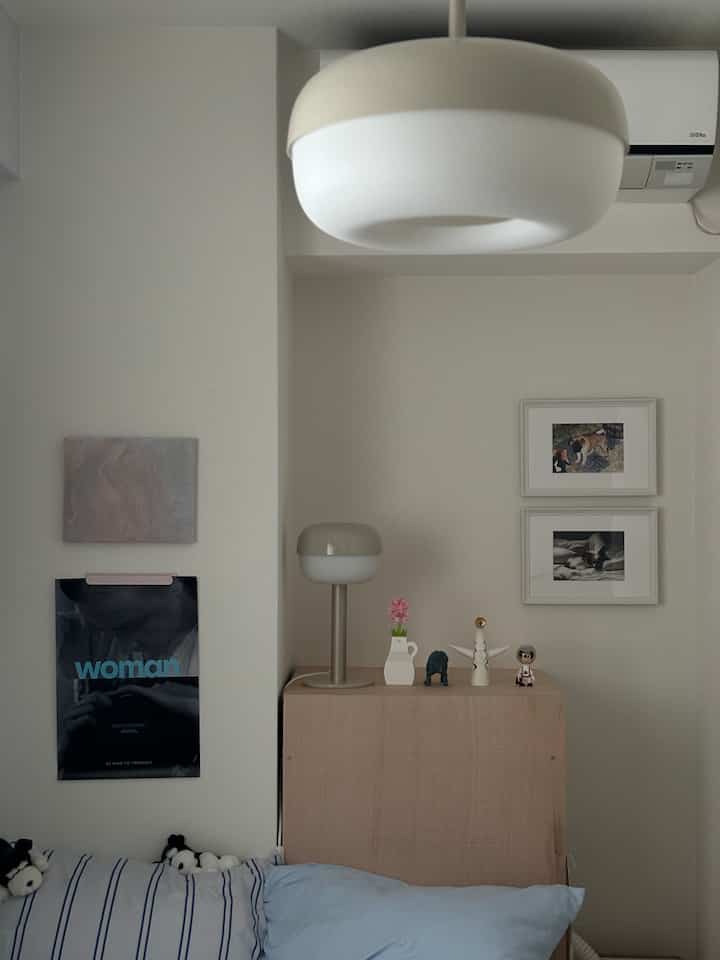 アイボリー調のナチュラルな寝室、木製キャビネットの上にテーブルランプとペットの写真が配置された印象的な空間