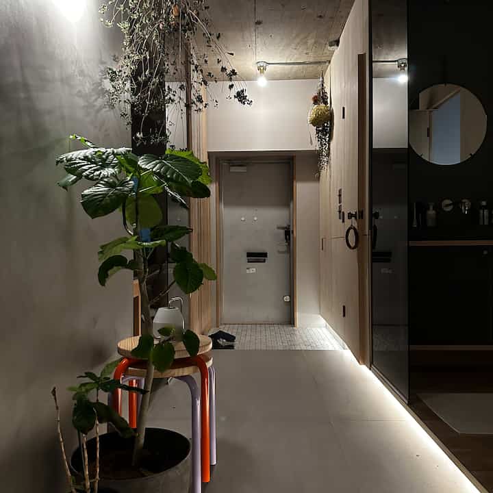 ナチュラルな木目調とタイルが際立つ広い玄関、観葉植物と丸い鏡が配置されたミニマルな印象のインテリア