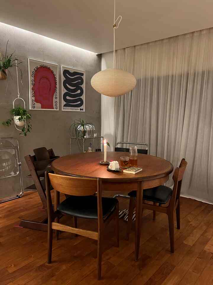 温かみのあるブラウンの木目調ダイニングルーム、丸いテーブルと4脚の椅子、ペンダントライト、カーテン、ポスターが配された雰囲気ある空間