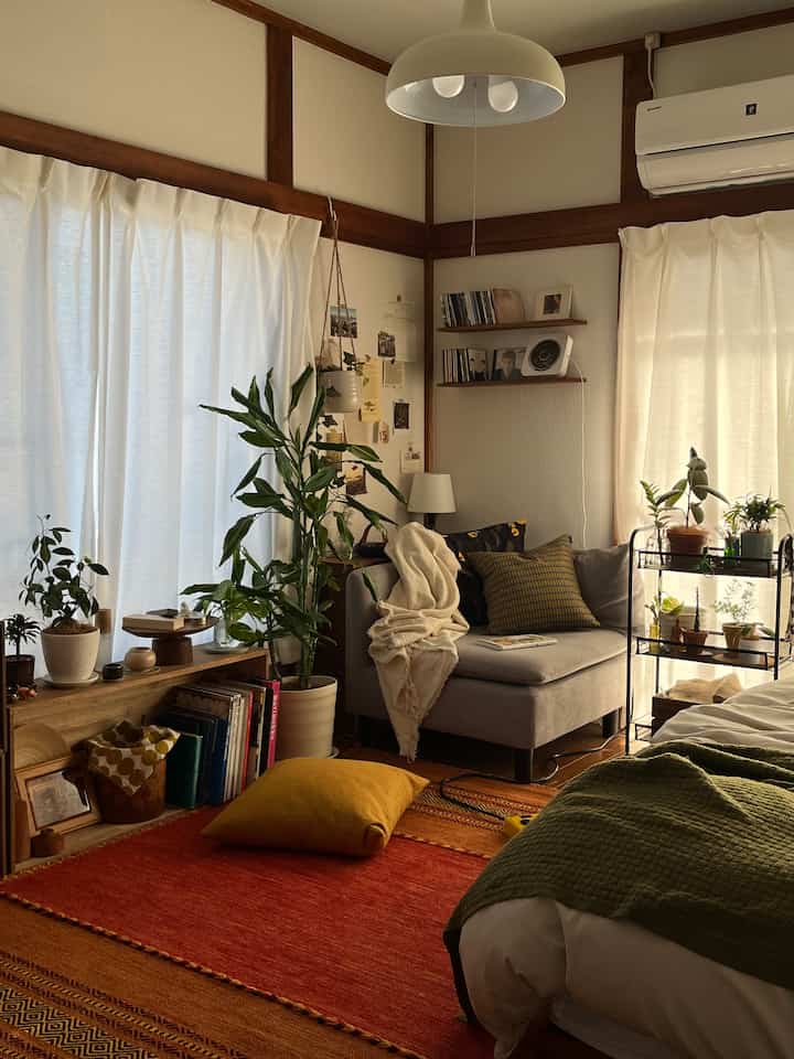 Warm natural-toned studio living room featuring red rug and various plants creating a cozy atmosphere