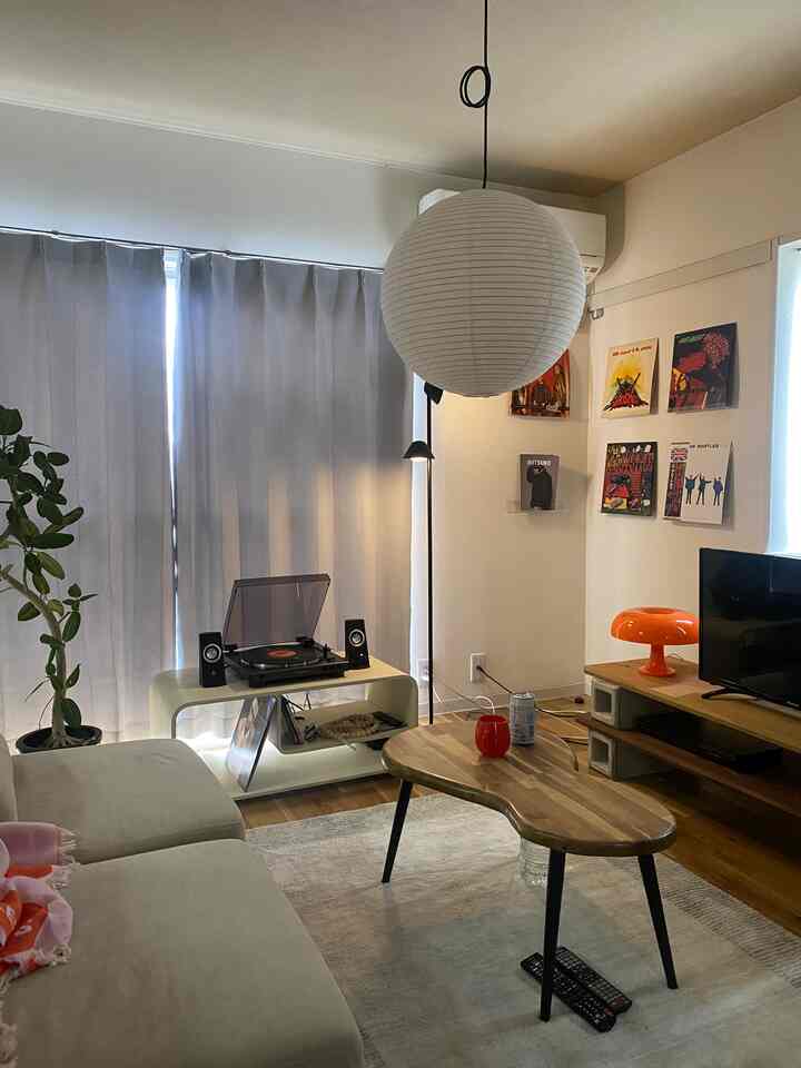 ナチュラルな色調の6畳リビング、ソファと個性的な木製コーヒーテーブル、ペンダントライトが配置された北欧風の印象的な空間