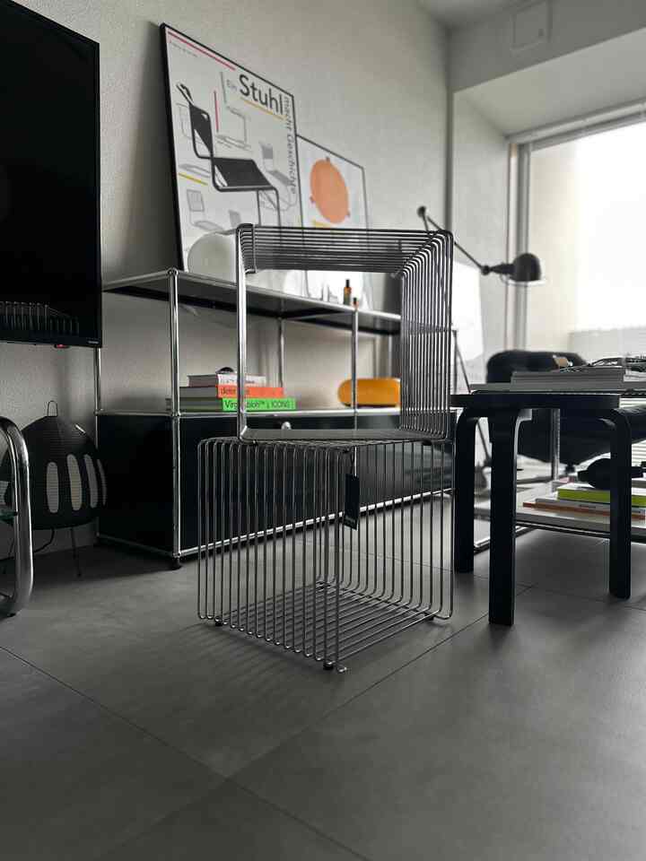 Modern living room with gray tiled floor, black metal furniture including wireframe stool and storage rack, featuring minimalistic design
