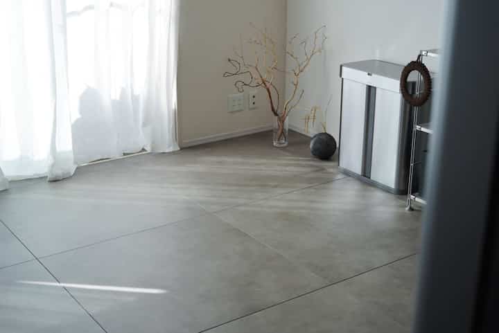 グレーのフロアタイルと白いカーテンがあるナチュラルな雰囲気のリビングの一角