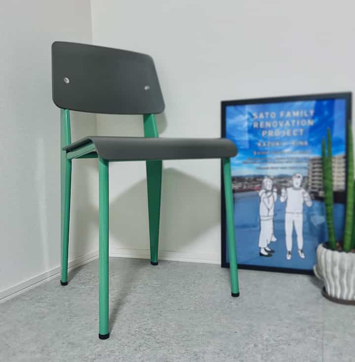 白い壁の背景に緑色の脚と黒い座面を持つシンプルな椅子が置かれたミニマルなリビングスペース