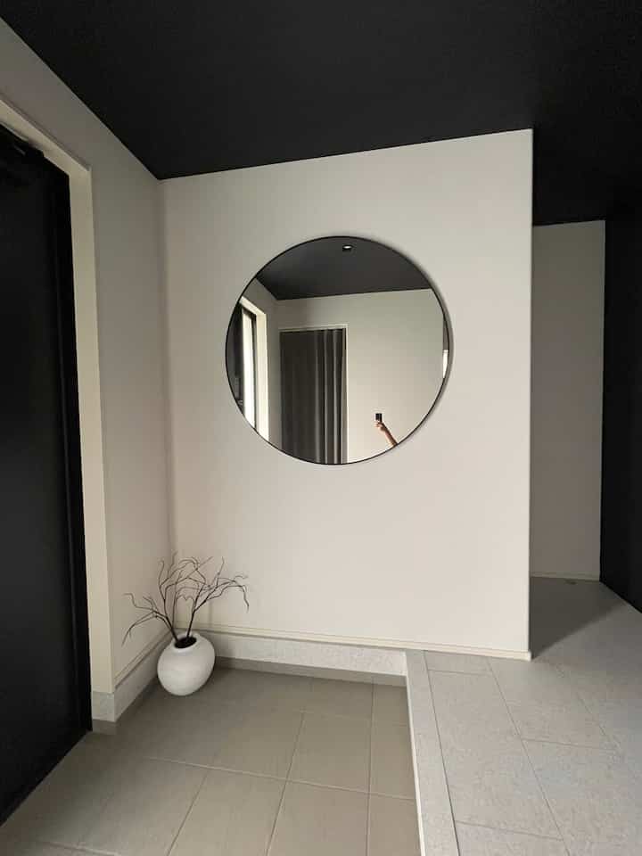 白い壁と黒い天井が調和するミニマルな玄関、丸い鏡とシンプルな花瓶が配置された清潔感のある空間