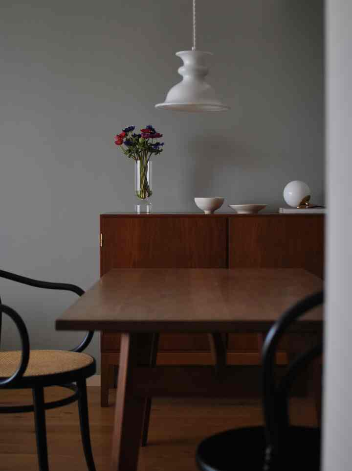 木目調と黒が調和するダイニング、シンプルな木製テーブルとペンダントライト、および花瓶が配された温かみのある雰囲気の空間
