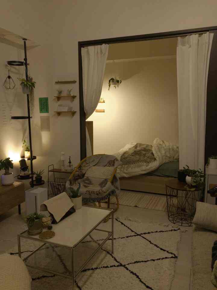 暖かい照明とナチュラルトーンの1LDKリビングと寝室がカーテンで仕切られた雰囲気のある空間