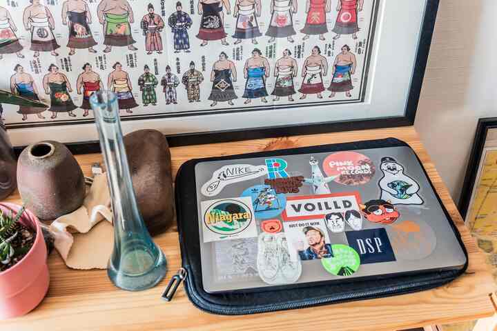 ナチュラルな木製の棚に多様なステッカーが貼られたMacBookが置かれた雰囲気のあるホームオフィス