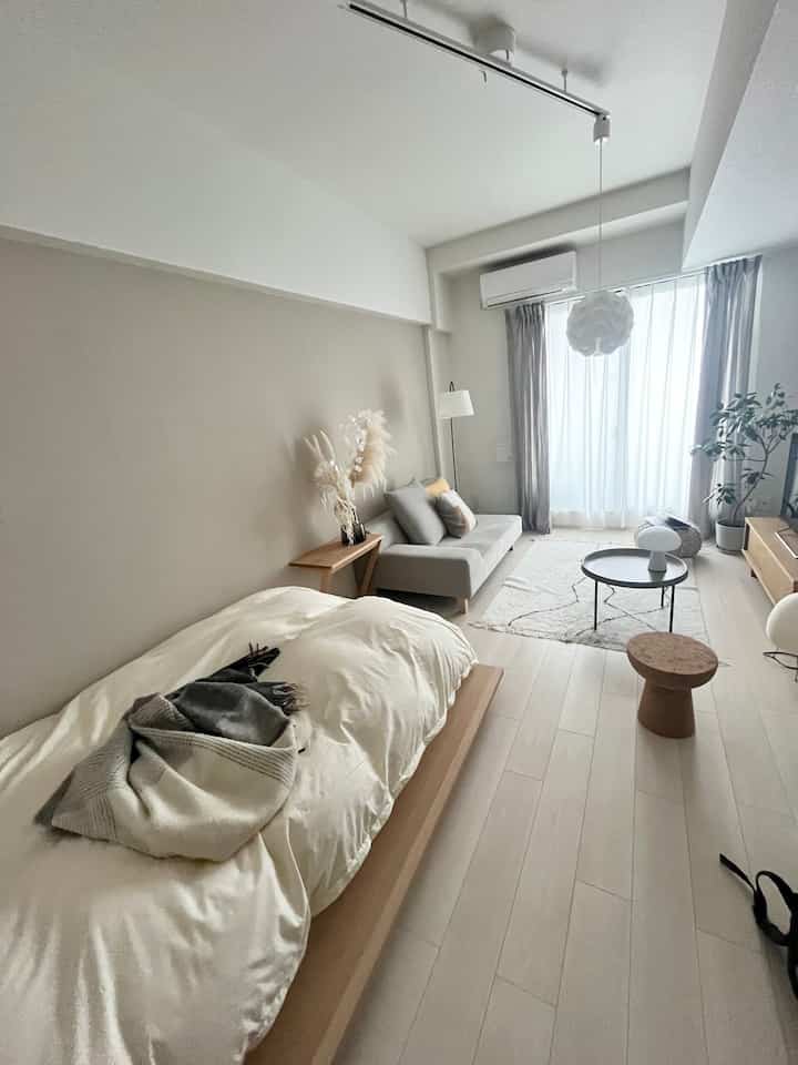 ベージュトーンと木製家具が調和した縦長のワンルーム寝室、シンプルで自然な雰囲気のインテリア