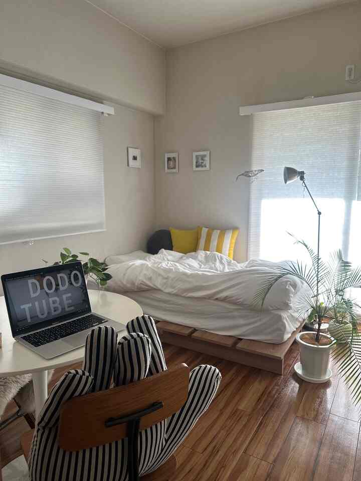 白と黄色のトーンのワンルーム、ノートパソコンや植物が配置されたシンプルで自然な雰囲気のインテリア