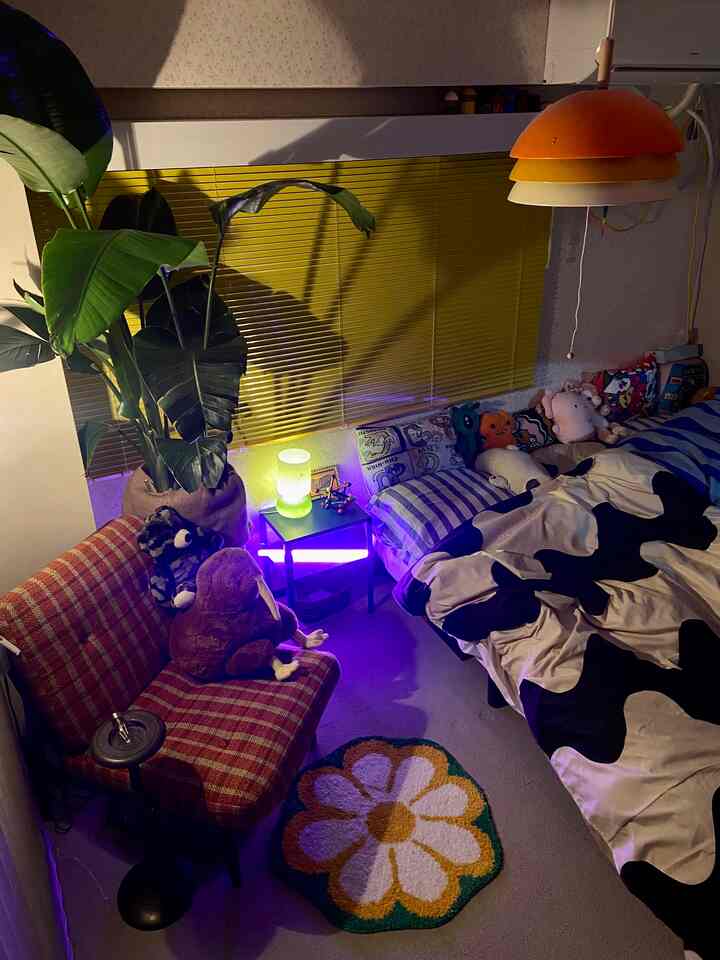 黄色いブラインドとヴィンテージ風の赤いソファ、花柄ラグが配置された寝室、白黒のベッドカバーが印象的な雰囲気のあるインテリア