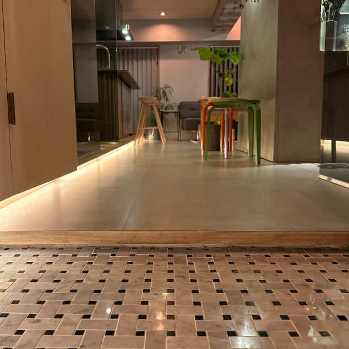 ナチュラルな木目調とタイル床が特徴のモダンな玄関、スツールと照明が配置された雰囲気のあるインテリア