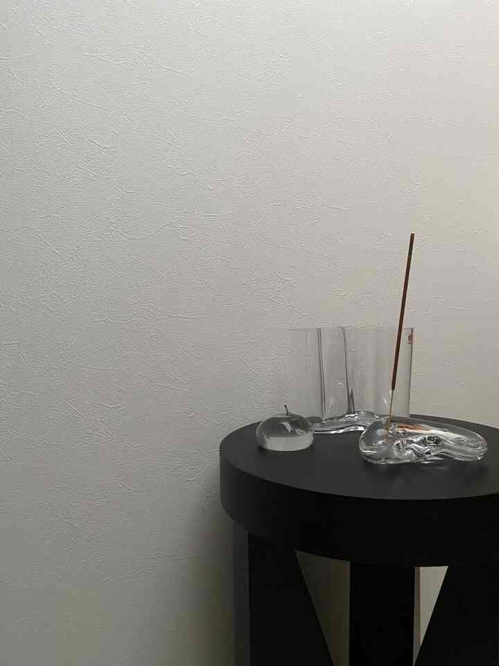 透明なガラスのオブジェが黒い円形スツールの上に置かれたシンプルな室内インテリア