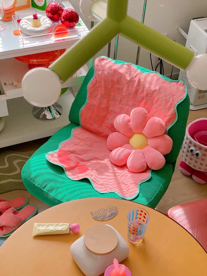 ピンクのクッションとオレンジ色のテーブルがある緑のアームチェアが配置された明るいレトロ風リビング