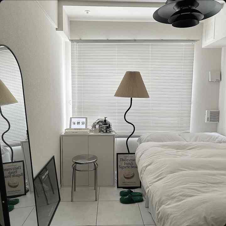 白を基調とした寝室、白いブラインドとフロアランプが配置された清潔感のあるモダンな空間