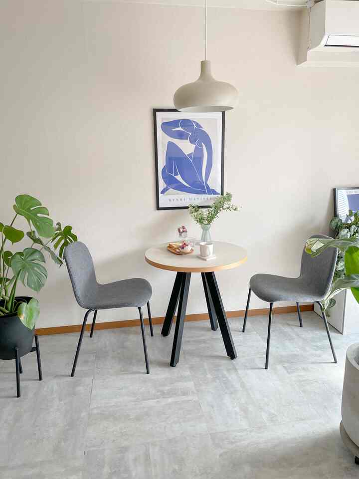 Beige and white toned compact dining space featuring a round dining table, two gray chairs, and a pendant light creating a clean interior