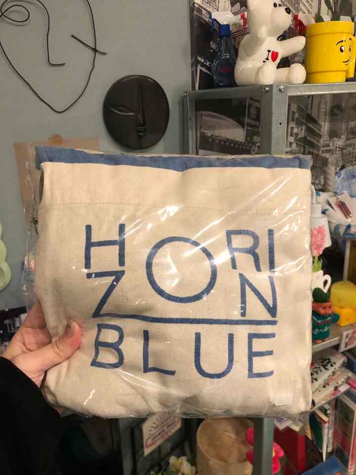 ブルートーンのエプロンが包装された状態で、キッチン用品の背景が見える空間