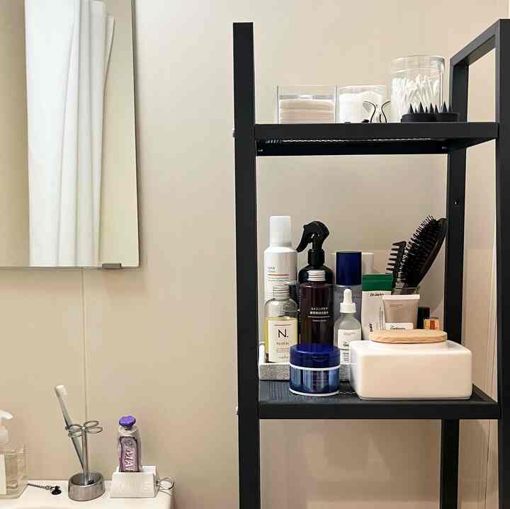 Ivory-toned bathroom featuring a black metal shelf neatly organized with various toiletries and grooming products