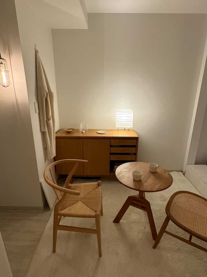 オーク材と白を基調としたジャパンディスタイルのリビング、Yチェアとキャビネットが配置され、居心地の良い照明のあるシンプルな空間