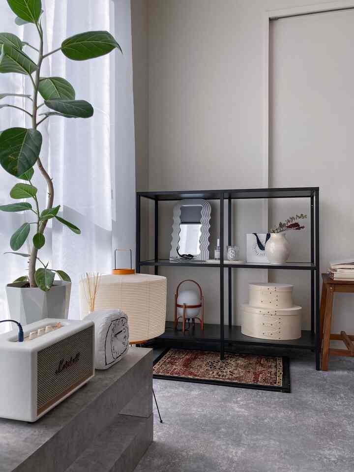 ベージュの壁とモダンなブラックの棚が配置されたシンプルで清潔感のある一人暮らしのリビング