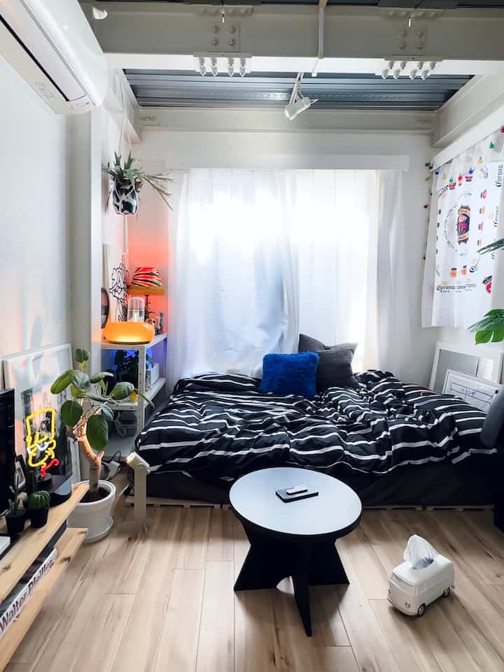 Bright white studio bedroom featuring black striped bedding, natural wood flooring, and cozy atmosphere