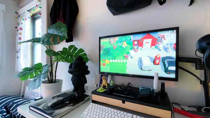 白い壁と天井が背景の6畳ワンルームのワークスペース、モニターとモニタースタンド、人工モンステラの植物が調和した狭いゲームルームのインテリア