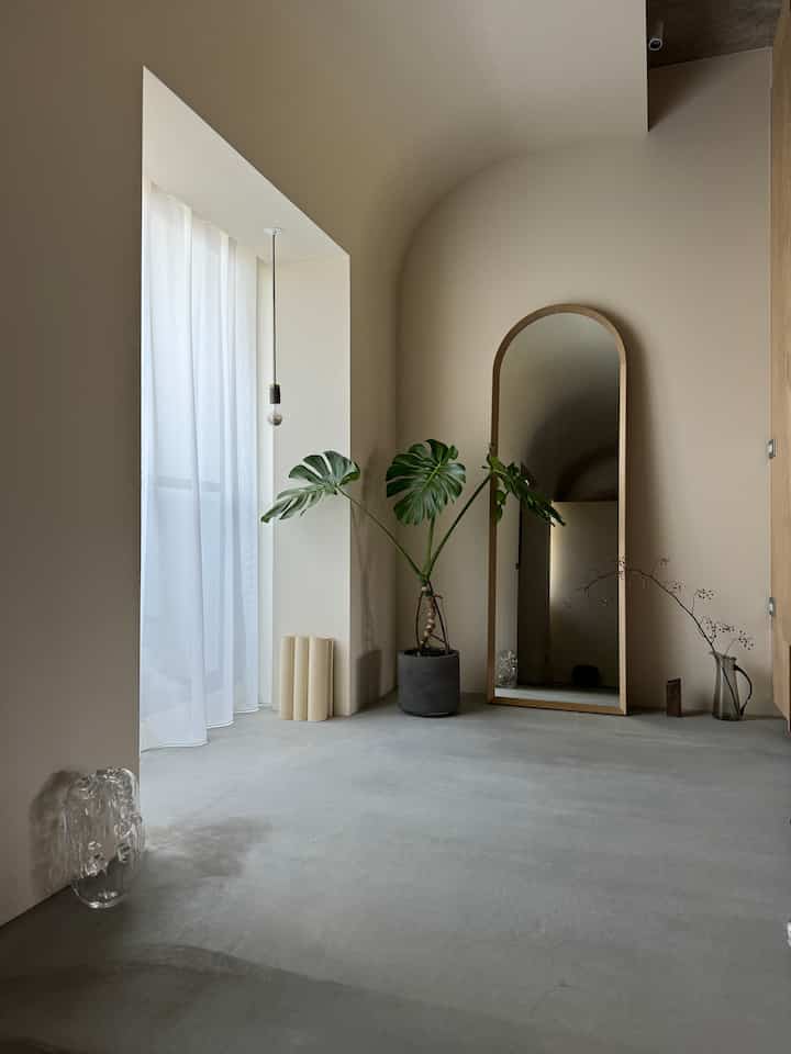 Beige-toned modern entrance space featuring an arch ceiling, large full-length mirror and Monstera plant in a minimalist setup