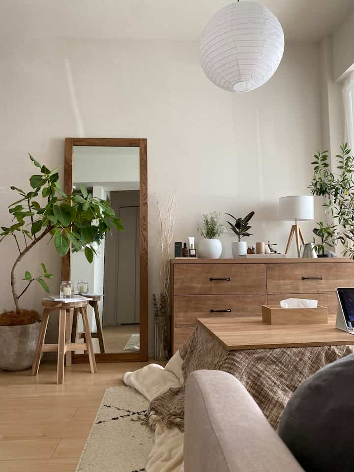 Natural wood tone and beige living room featuring a large mirror, green plants, and a cozy kotatsu table creating a warm atmosphere