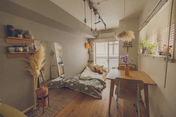 温かみのあるナチュラルカラーのワンルーム、ダイニングテーブルと寝具が配置された雰囲気のあるインテリア。