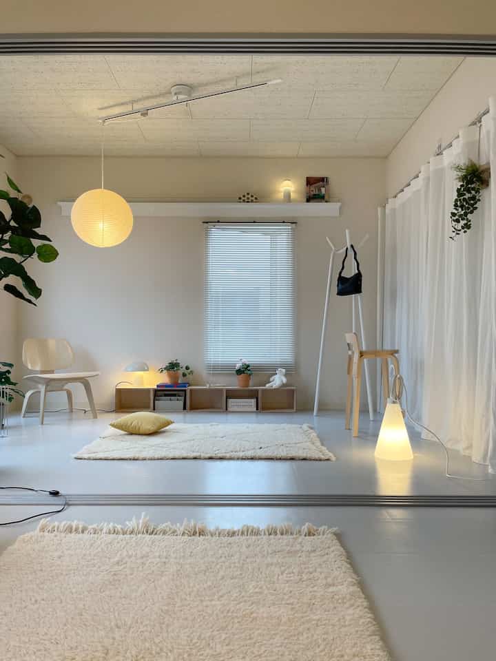 白とナチュラルな色調のリビング、木製家具とペンダントライト、フロアランプが配されたシンプルな空間