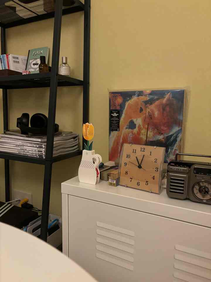 淡い黄色の壁の空間に、白い鉄製キャビネットの上に花瓶、時計、レトロなラジオが配置された雰囲気のあるインテリア