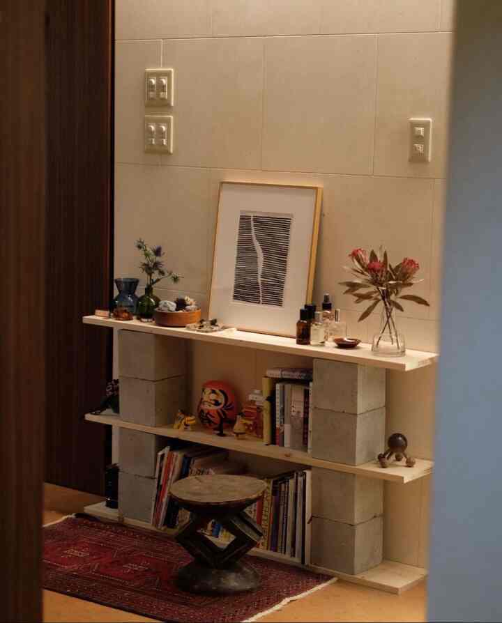 ナチュラルカラーの壁に設置されたDIYコンクリートブロックの棚とヴィンテージラグがある雰囲気のあるインテリア