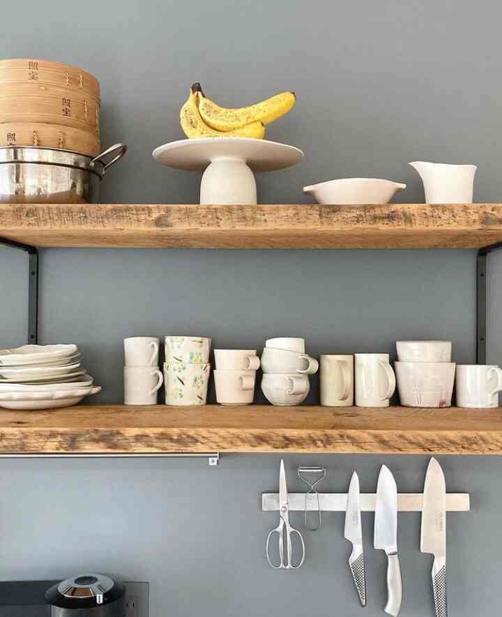 グレーの壁と木目調の棚にカップや皿が整然と置かれたシンプルなキッチン空間