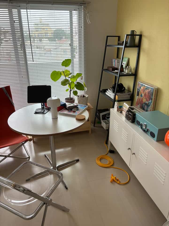 A small room with yellow walls and white furniture in mid-century modern style, featuring plants on the central table and shelves, creating a cozy atmosphere