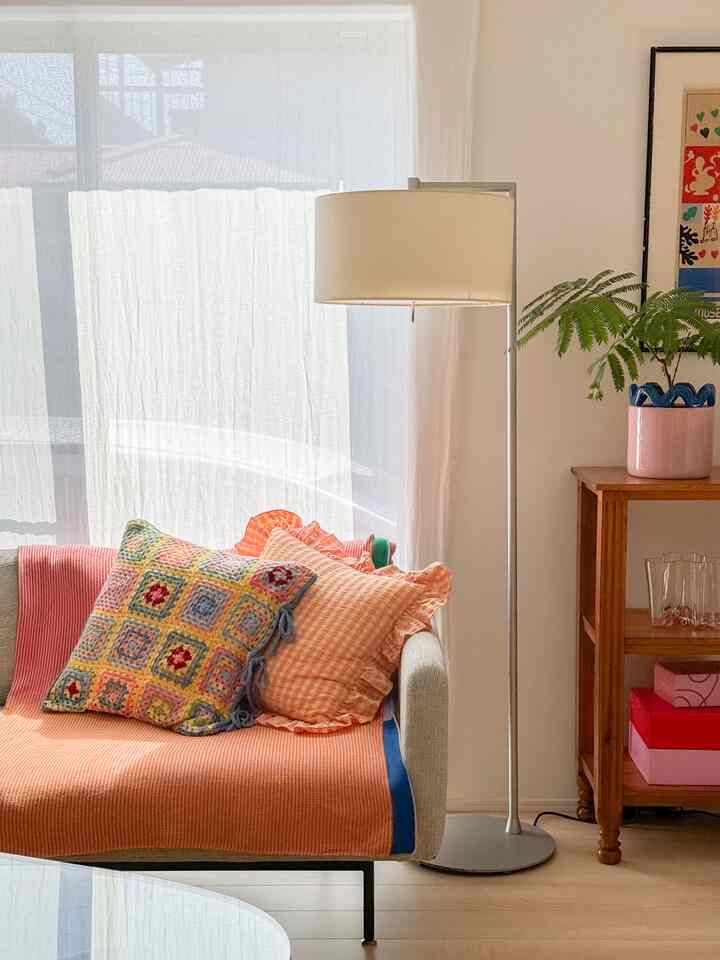 温かみのあるオレンジ色のリビング、ベージュのソファにオレンジのブランケットとクッションが配置され、ナチュラルウッドのサイドテーブルが温かい雰囲気を演出する印象的な空間