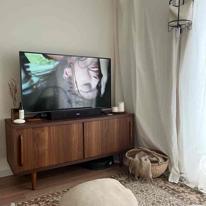 ナチュラルな色調のワンルームリビングルーム、木製のテレビ台とベージュのカーテンが配置されたシンプルで居心地の良い空間