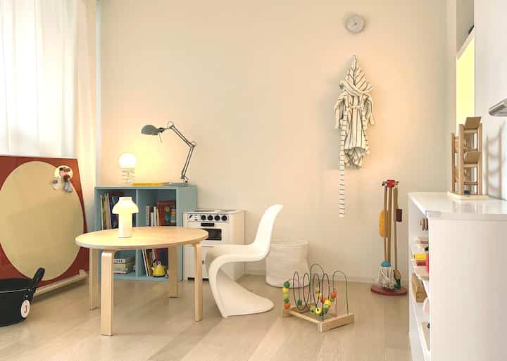 White and wood tone kids' room featuring child-sized table, chair, toys, and lamps with a clean, natural atmosphere