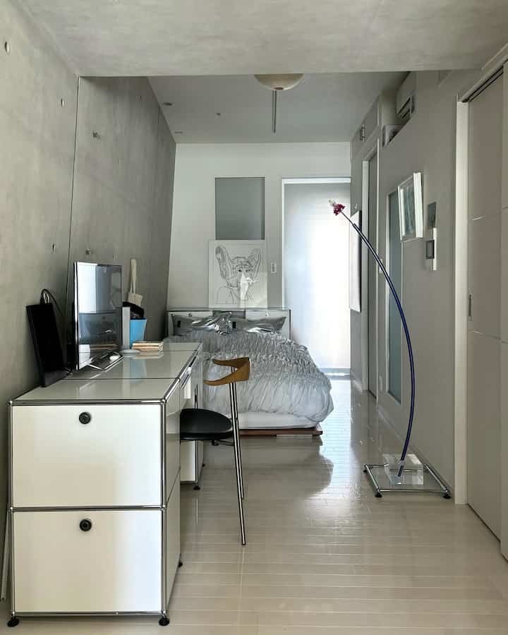A narrow bedroom in white and gray tones featuring a modern, minimal desk and bed setup