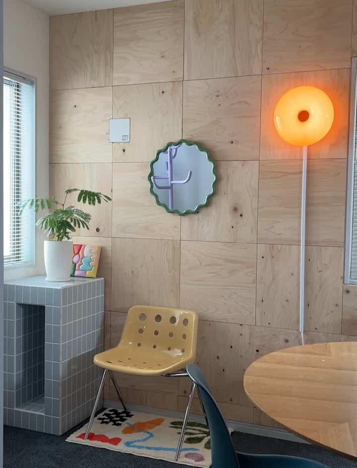 Wood tone paneled dining room with bright orange wall lamp and yellow dining chair, creating a warm atmosphere