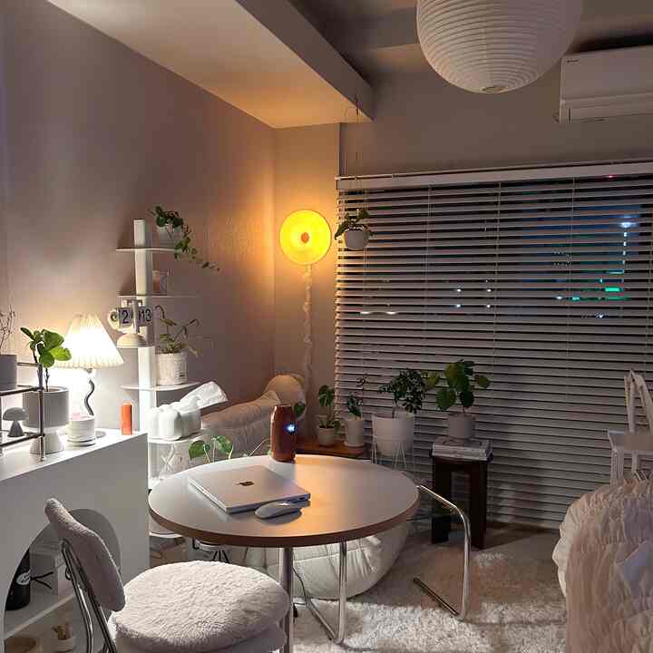 暖かいオレンジ色の照明と植物がある一人暮らし向けのナチュラルモダンなリビング、丸テーブルと快適な椅子が配置された印象的な空間