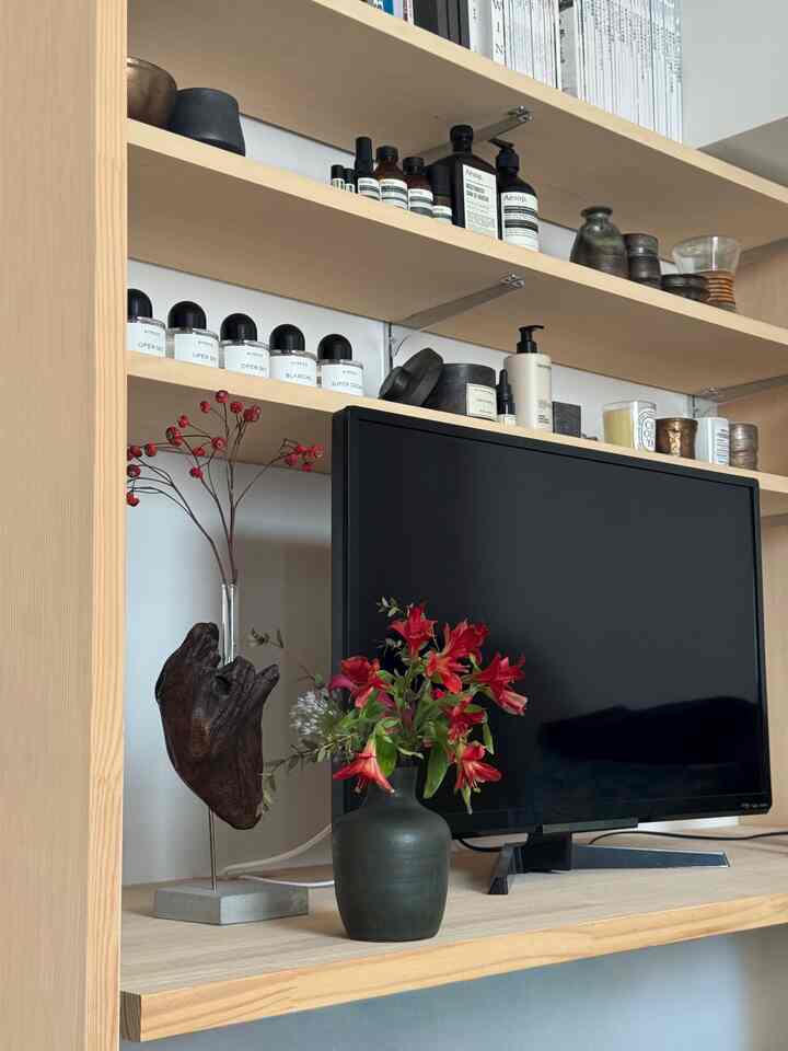 ナチュラルな木目調のリビング、黒いテレビ台と赤い花が生けられたダークな花瓶が配置された雰囲気のあるインテリア