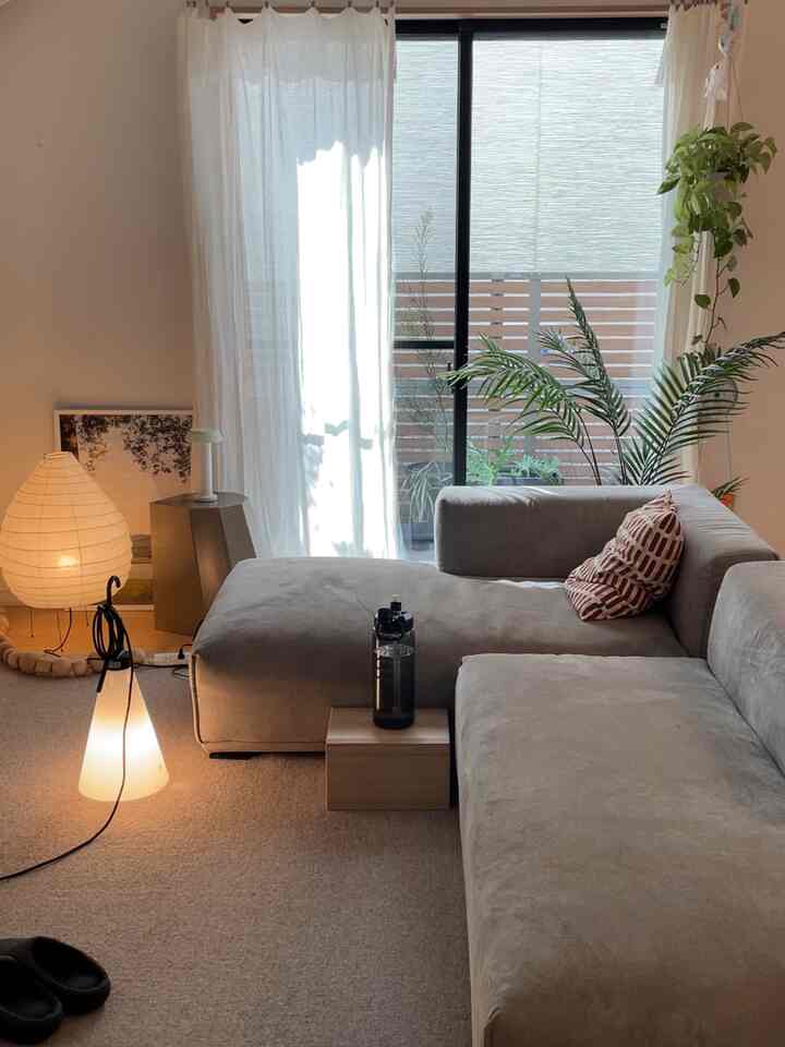 Calm gray-toned living room featuring large sofa, floor lamps, and plants by the window in a natural modern interior