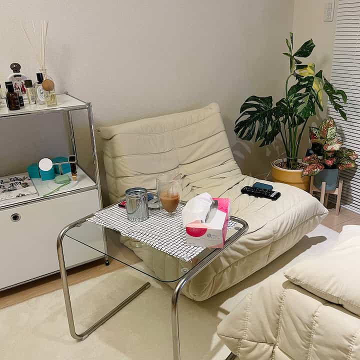 白と緑のトーンのリビング、クリーム色のソファとガラスのサイドテーブル、観葉植物が配置されたシンプルなインテリア