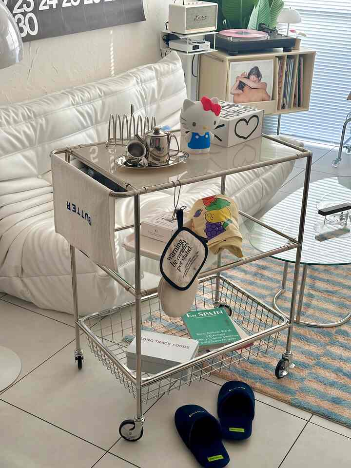 ホワイトとシルバートーンのリビング、ガラス棚のトロリーと白いレザーソファが配置された清潔感のあるモダンな空間