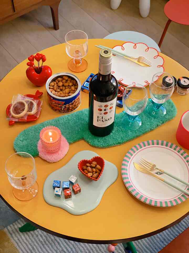 Cozy dining space featuring a yellow round table with a green table runner, wine bottle, various plates, and wine glasses