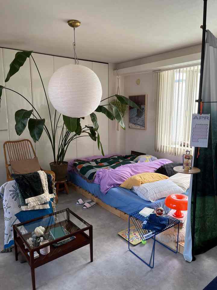 白とナチュラルカラーの寝室、大きな植物と木製ベッドが配置された雰囲気のあるモダンな空間