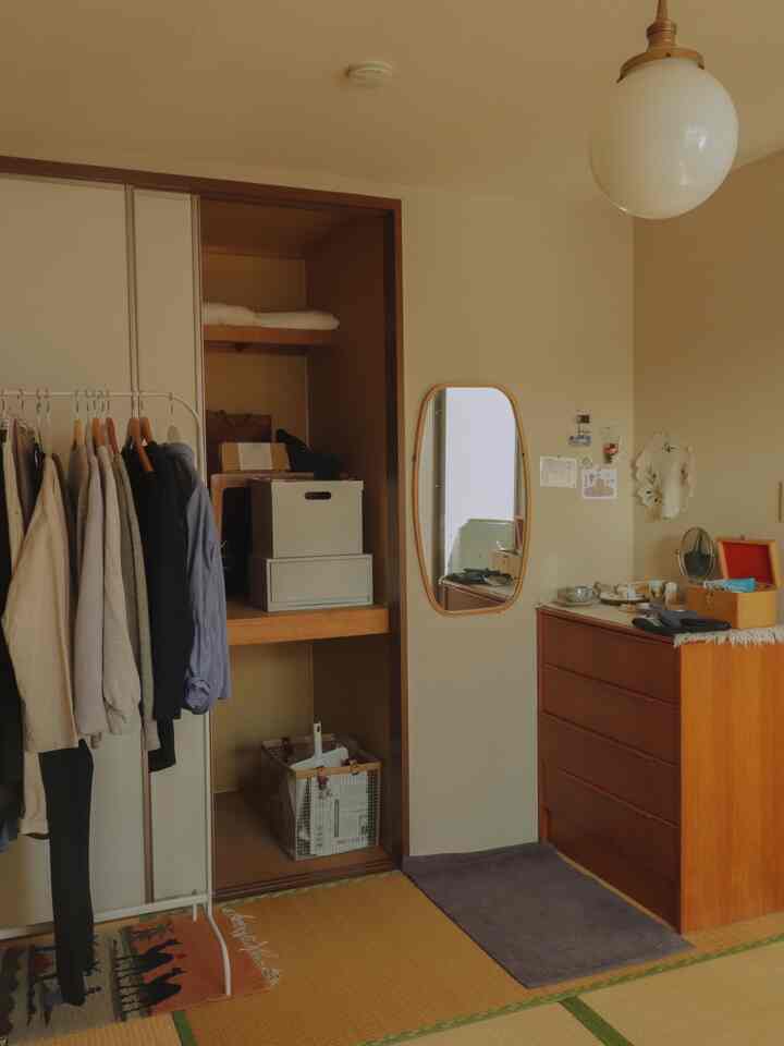 ナチュラルカラーのコンパクトな部屋、洋服掛けと開かれたクローゼットが配置された清潔感のある収納空間
