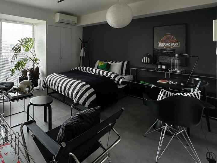 ブラックとホワイトのトーンの寝室、ストライプのベッドリネンとアームチェア、ポスターが配置されたミニマルでモダンな雰囲気のインテリア