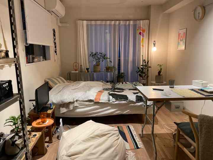 Cozy bedroom with beige walls and natural wood-tone flooring, featuring a central bed and desk in a compact room
