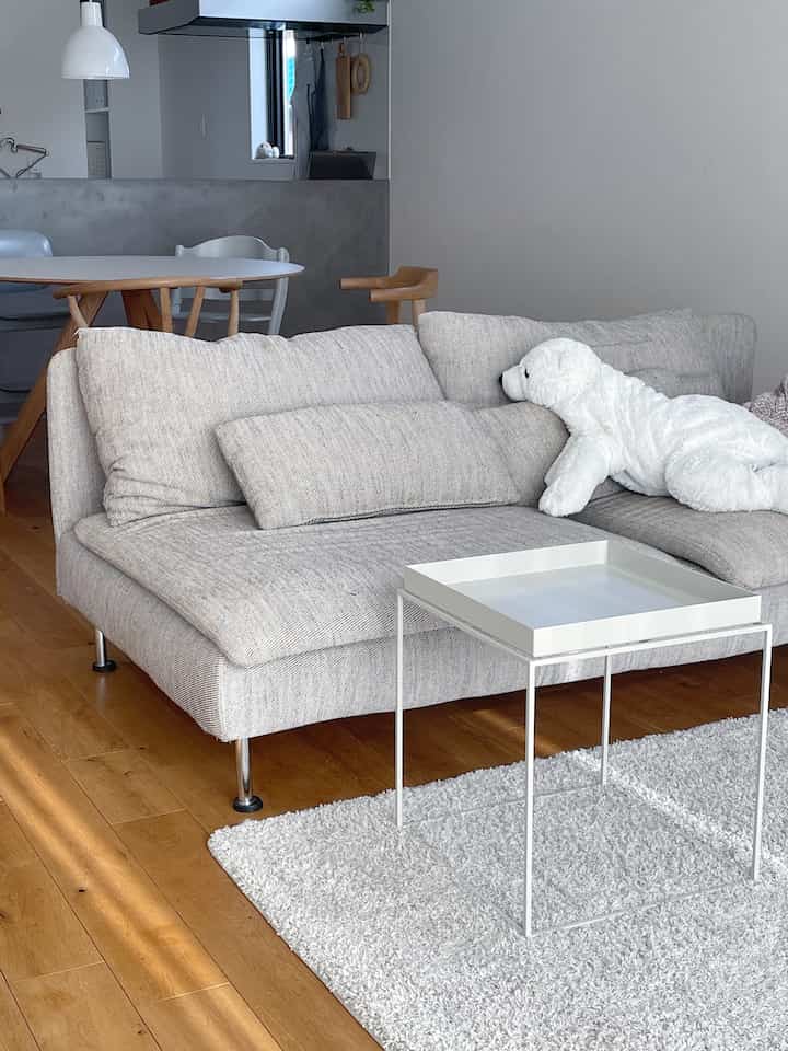 白とグレーのトーンのリビング、ライトグレーのソファと白いサイドテーブルが配置されたシンプルでナチュラルなインテリア